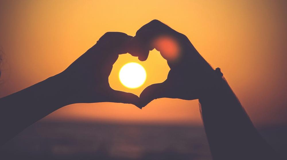 Image of hand heart gesture behind a sunset © Mayur Gala/Unsplash